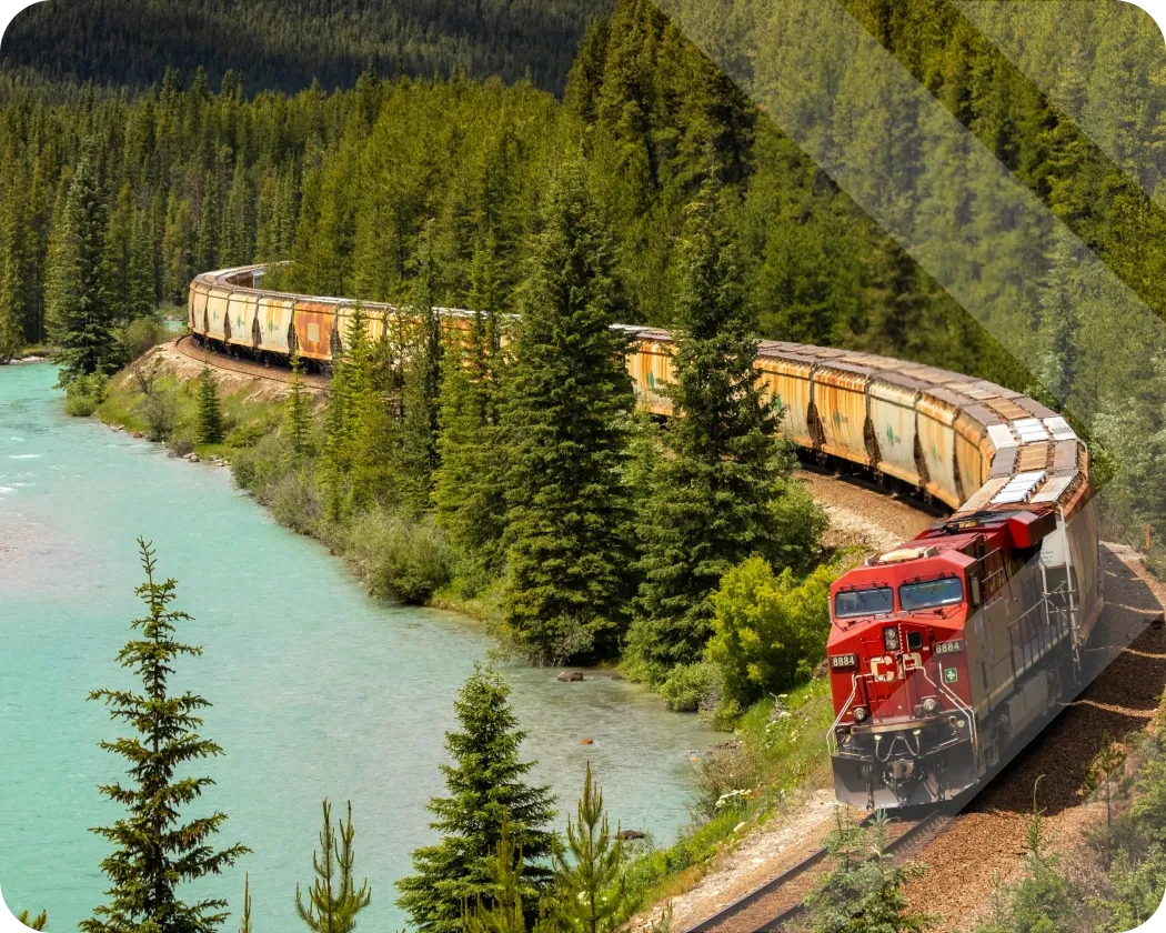 A train hauling freight on a scenic mountain pass surrounded by forest and water.