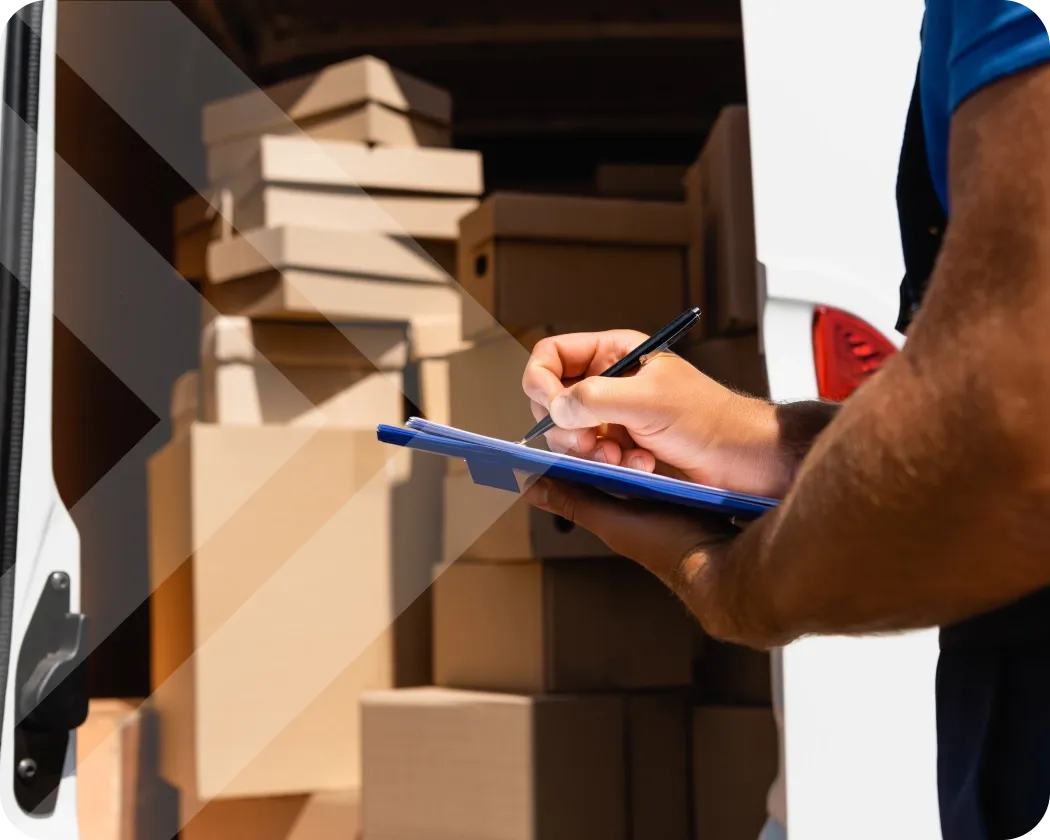 A person marking something on a clipboard in front of a van full of boxes.
