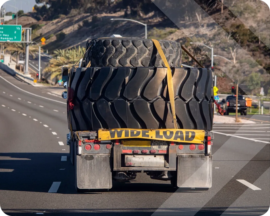 A vehicle on the road carrying several very large tires with a banner reading “wide load” attached to the back.