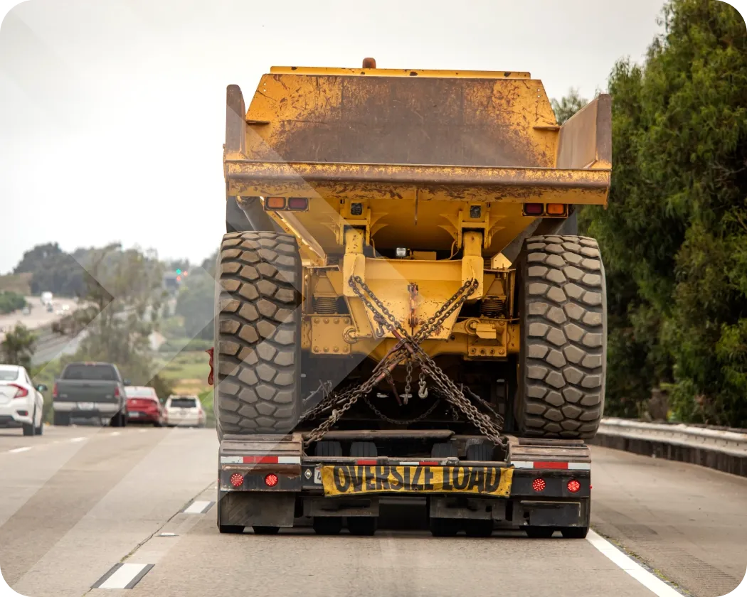 A truck on the road carrying a large vehicle, with an “oversize load” banner on the back.