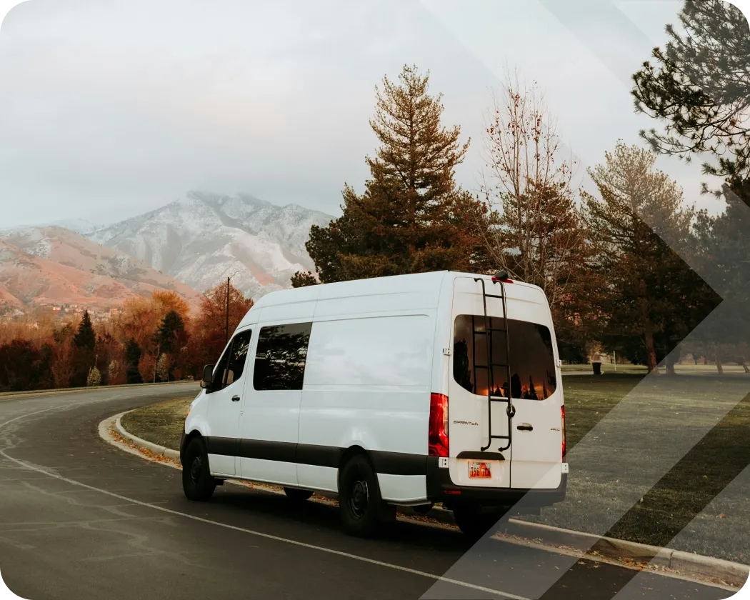 A sprinter van driving down a scenic mountainside road.