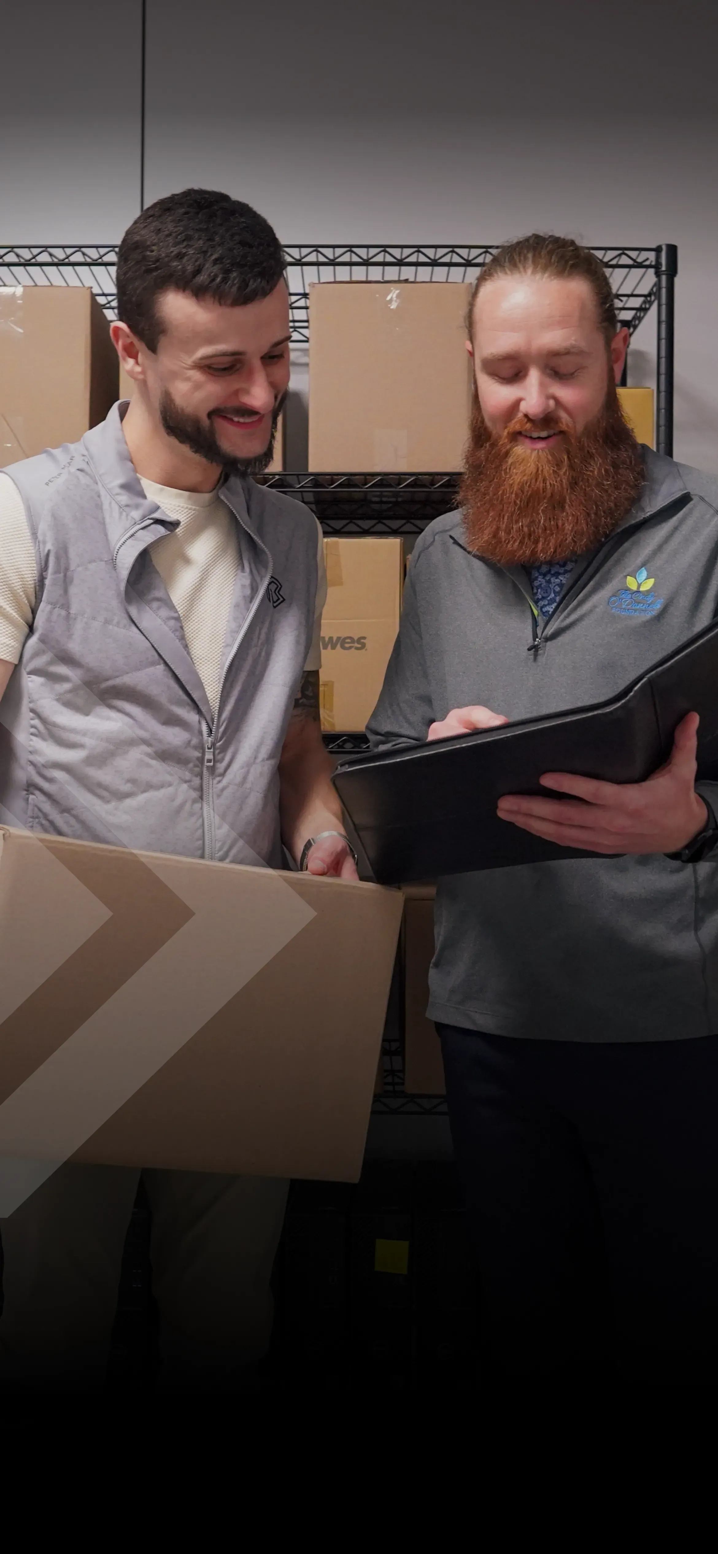 Two customers discuss shipments in a warehouse full of boxes.