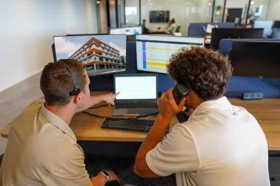 Two people on a phone call together with one of them pointing at a laptop screen